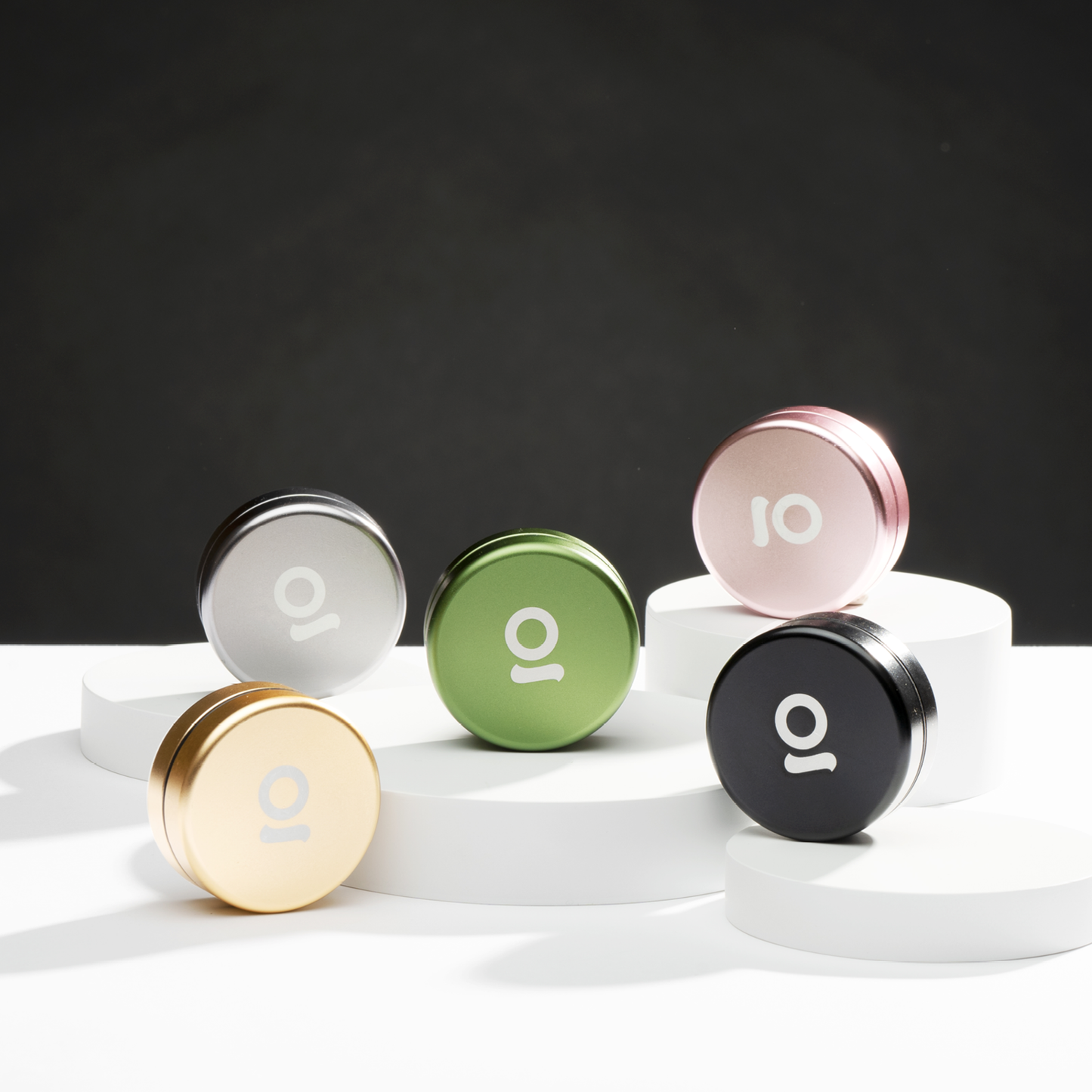 Five round containers with different colored lids on a white surface against a dark background
